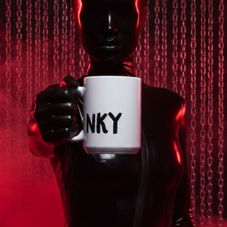 Kinky Mug: A glossy white mug with bold NKY print, held by a latex-clad figure amidst red-lit chains