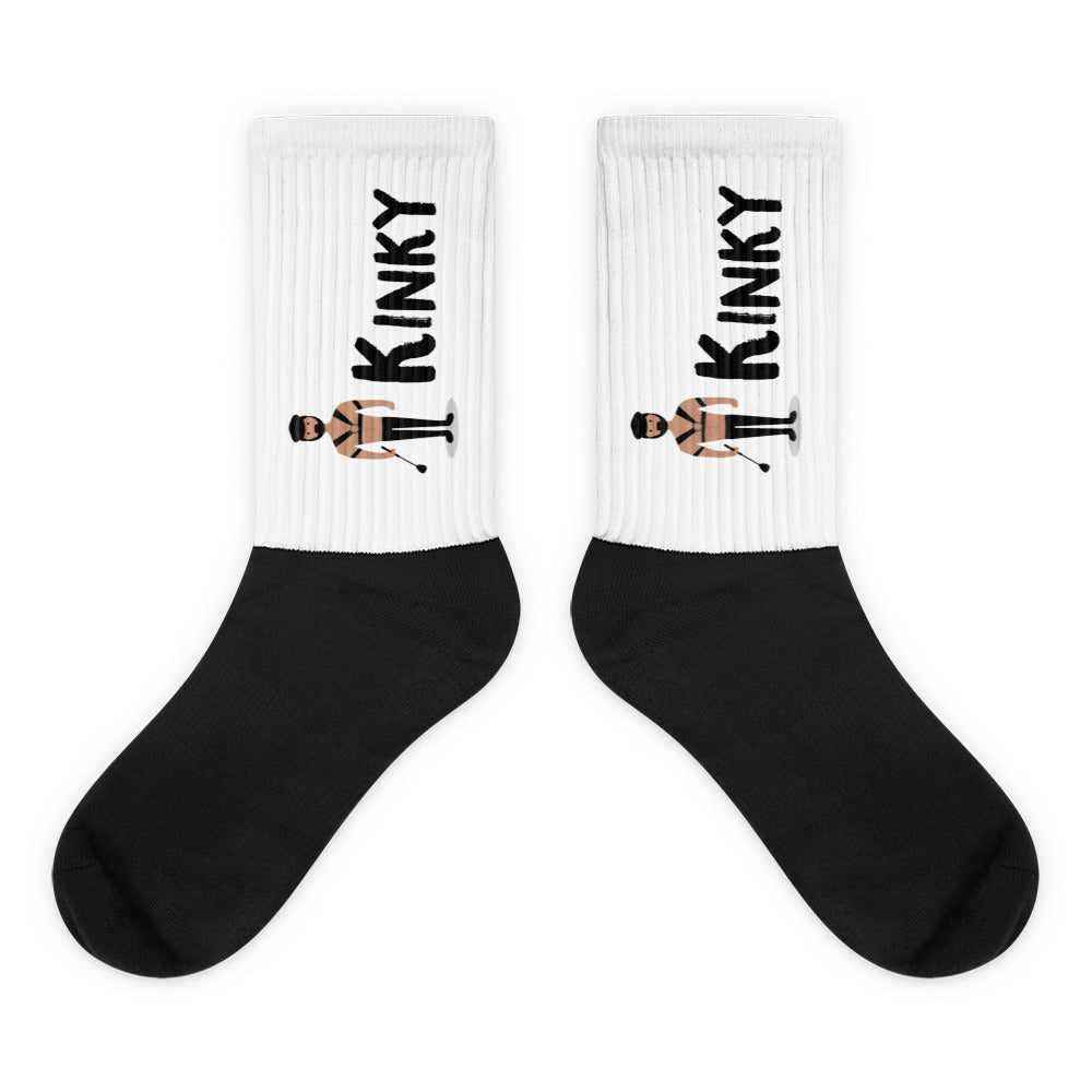 Pair of crew socks with black feet and white cuffs reading “KINKY” beside harnessed figures