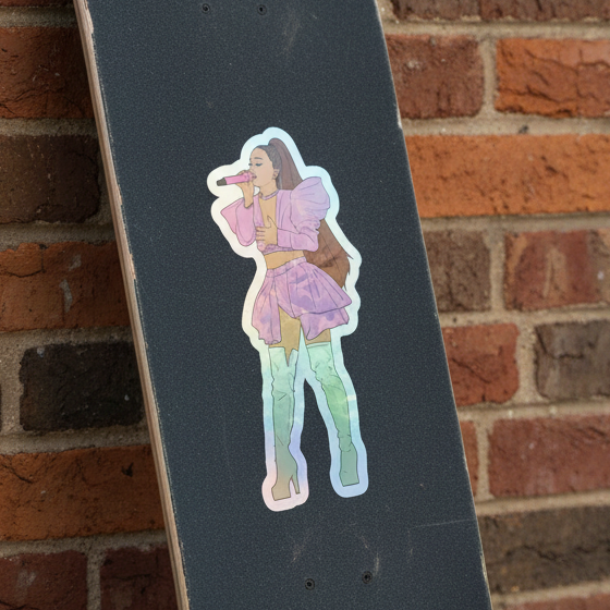 Skateboard with black grip tape decked out in Ariana Grande holographic stickers—her in purple, blue boots, belting into a red mic.