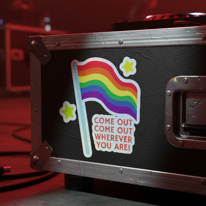 Come Out Come Out Holographic Sticker on a black metal road case, with rainbow flag, two yellow stars, and “COME OUT COME OUT WHEREVER YOU ARE!”; red stage lighting in the queer party backdrop.