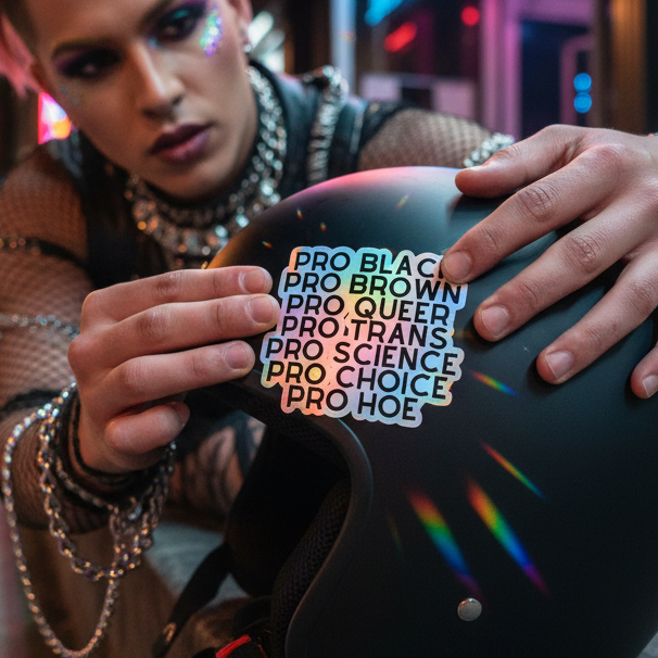 Pro Hoe (Black Text) holographic sticker shines with rainbow vibes as a queer person in glitter places it on a black helmet.