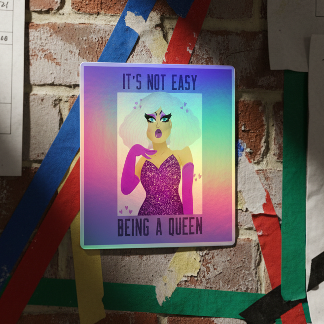 Square poster on brick wall shows "It's Not Easy Being A Queen Holographic Stickers": femme drag queen, white hair, purple gloves, sparkly dress, rainbow backdrop with shimmer and colored tape.