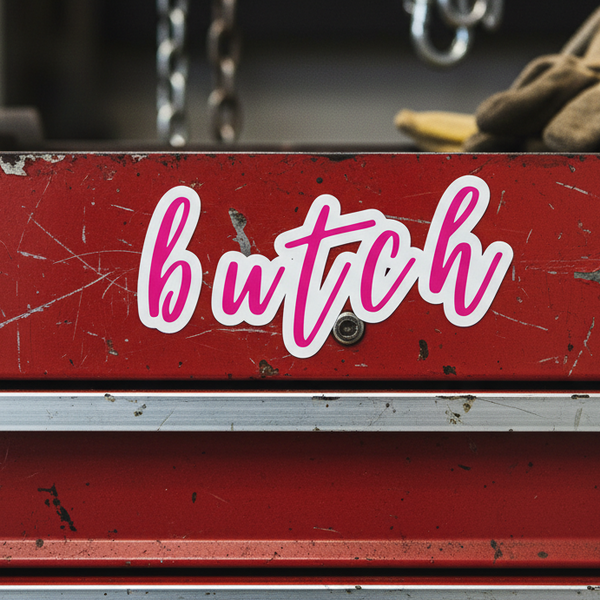 Red metal toolbox with a worn look, featuring a “butch” pink cursive sticker; brown work glove and chains in the background.