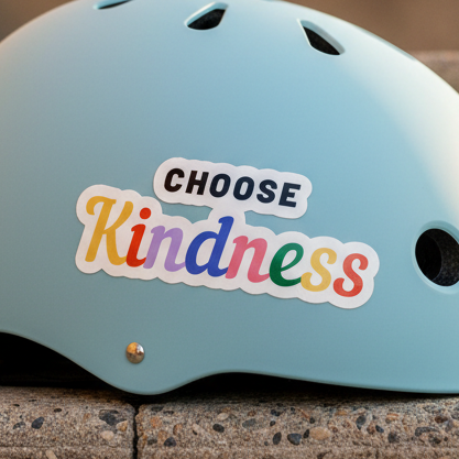 A light blue helmet featuring a bubble-free sticker: “CHOOSE” in bold black caps, “Kindness” in rainbow gradient script.