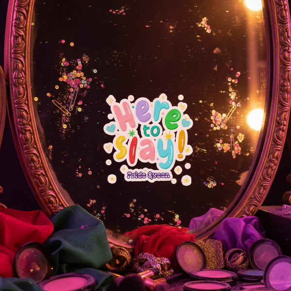 “Here to Slay!” Pride Queen sticker displayed on an ornate mirror among makeup and colorful fabric