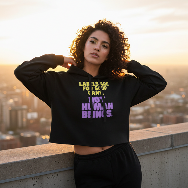 Crop hoodie with bold yellow and purple text, “Labels are for soup cans. Not human beings.” person poses at sunset rooftop