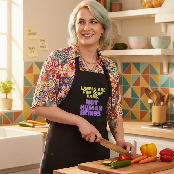 Person slicing vegetables while wearing a black apron reading “Labels Are for Soup Cans, Not Human Beings.”