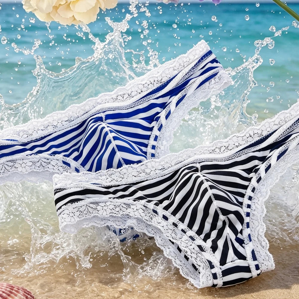 Two low-rise striped lace briefs displayed on wet sand amid splashing seawater