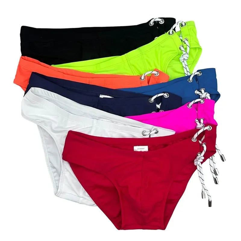 Stack of colorful lace-up swim briefs in black, lime green, orange, navy, blue, white, pink, and red