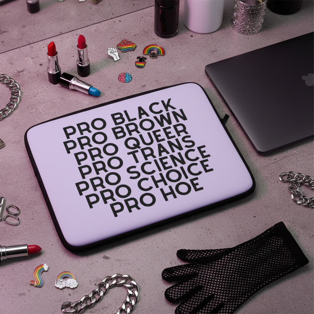 Laptop sleeve with bold black text reading: "Pro Black, Pro Brown, Pro Queer, Pro Trans, Pro Science, Pro Choice, Pro Hoe," surrounded by lipsticks, rainbow pins, chains, a glove, and a MacBook.