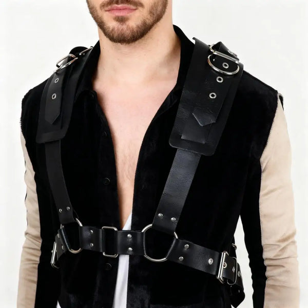 Cropped model wearing a black leather chest harness with straps, rings, and metal studs