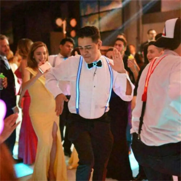 Front-facing person in a white shirt wearing blue glowing LED suspenders at a party