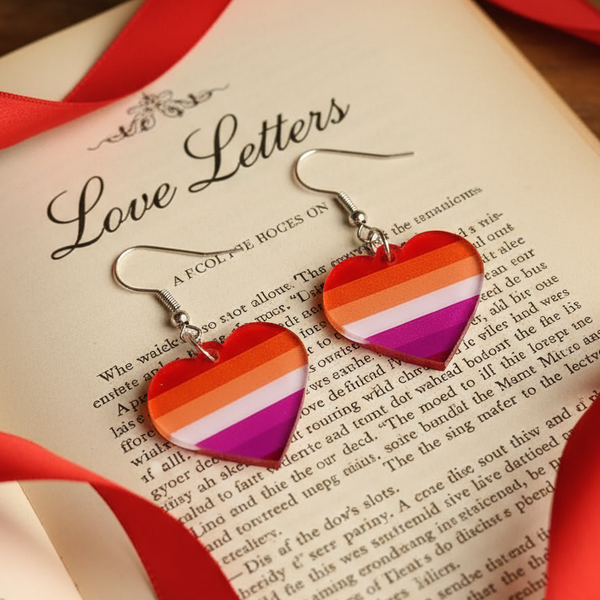 Rainbow-striped heart dangle earrings on an open “Love Letters” book with red ribbon
