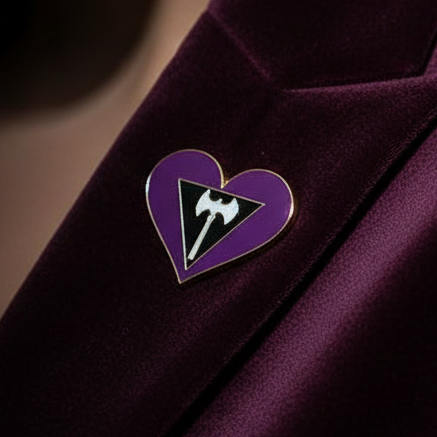 Close-up of a purple heart enamel pin with a labrys symbol on dark fabric