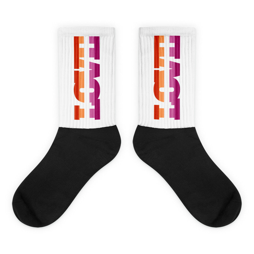 Pair of crew socks with black feet and white ribbed cuffs reading “LOVE” in orange and magenta