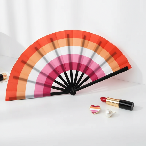 Open folding fan with orange, pink, white, and red stripes beside lipstick and heart pin