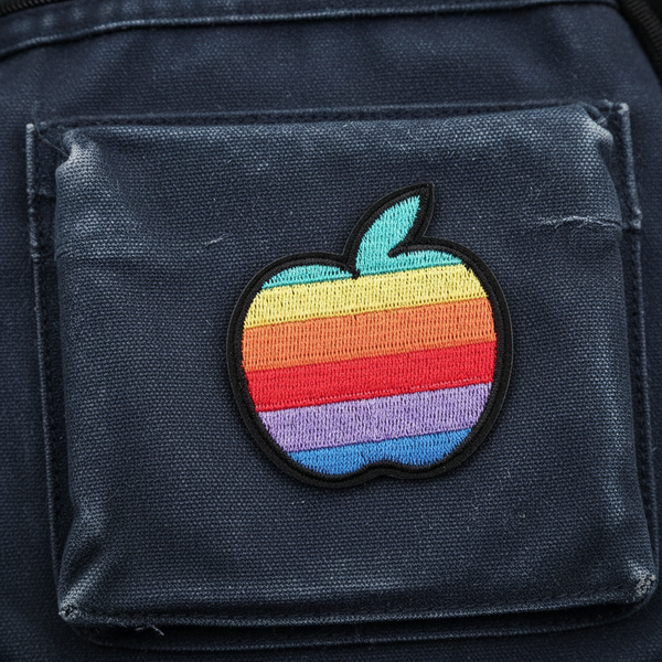 LGBT Apple iron-on embroidered patch in the iconic rainbow-striped Apple logo, sewn onto a dark blue or black fabric pocket.