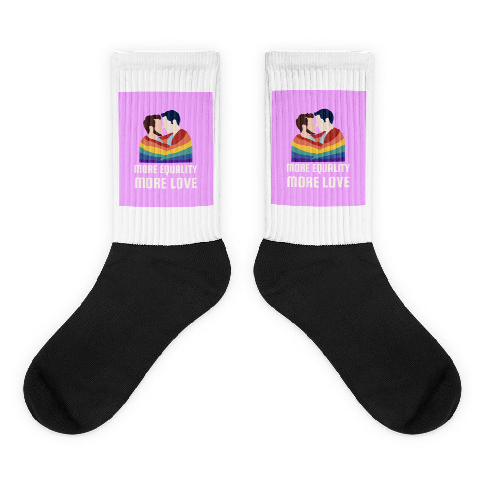 Pair of black-and-white socks with two men kissing beneath a rainbow and “MORE EQUALITY MORE LOVE” text