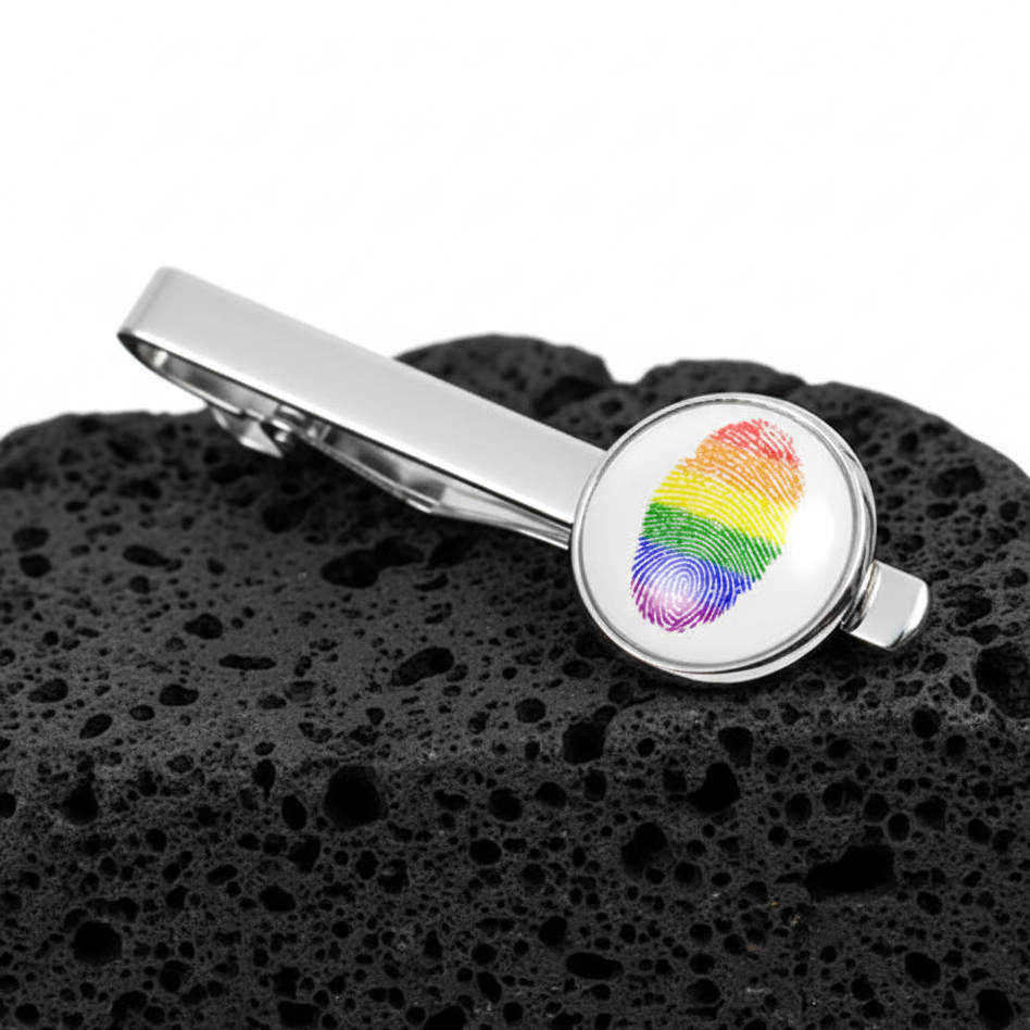 Silver LGBT tie clip with a rainbow fingerprint at its round end pops against textured black volcanic rock—a proud