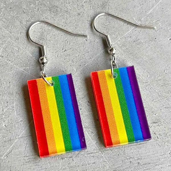 Pair of rectangular rainbow Pride flag acrylic drop earrings on a silver surface