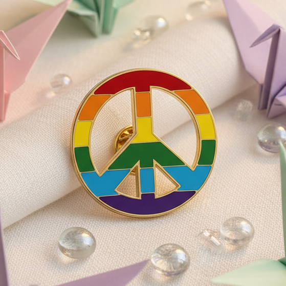 Rainbow-striped peace symbol enamel pin with a gold-tone outline on cream fabric