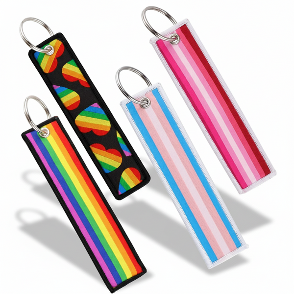 Four embroidered pride-flag keychains with metal rings, including rainbow, heart, trans, and pink stripes