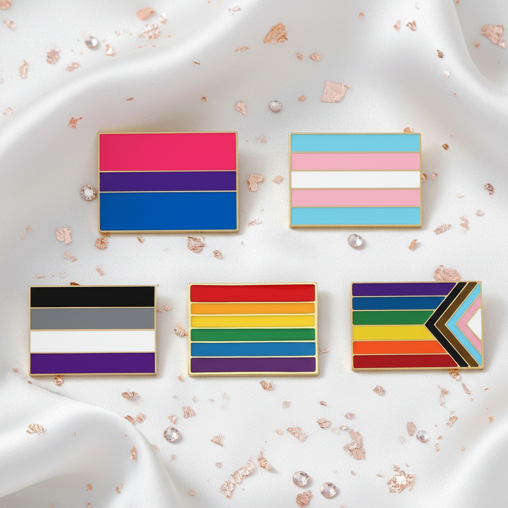 Five rectangular pride flag enamel pins arranged on white satin with rose-gold confetti