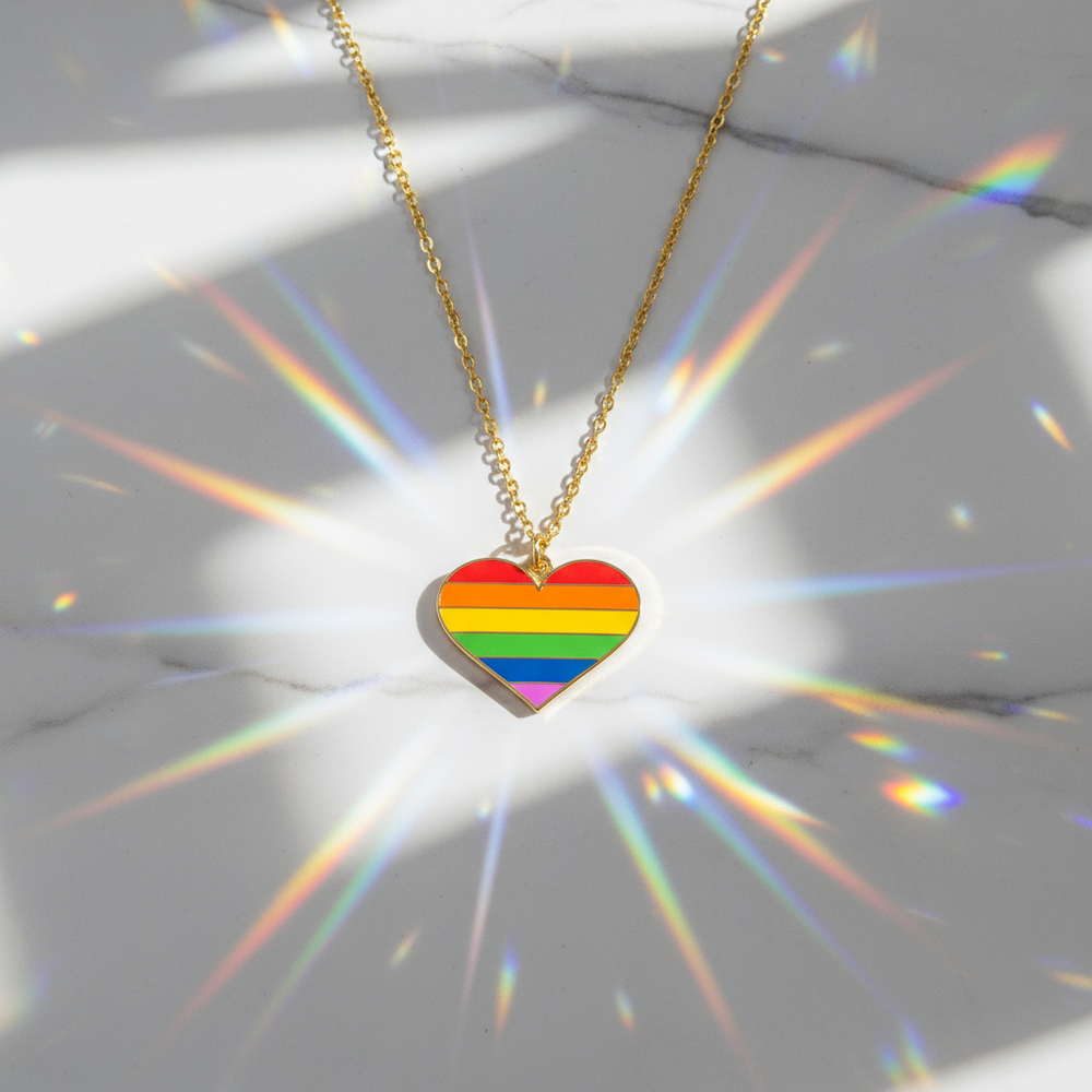Gold-tone chain necklace with a rainbow-striped heart pendant on a reflective surface