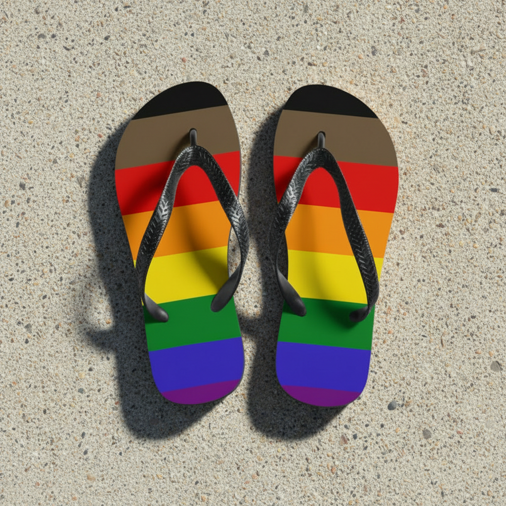 Pride Progress flip-flops with black straps, rainbow plus brown and black inclusive soles, pop on speckled concrete