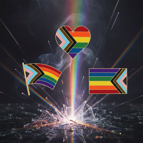 Three Progress Pride enamel pins—a heart, flag, and rectangle—float above rainbow-lit broken glass