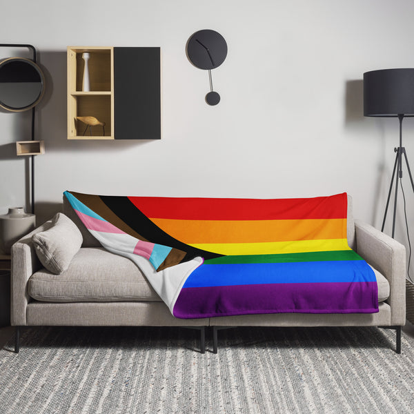 Progress Pride flag blanket draped across a gray sofa in a modern living room