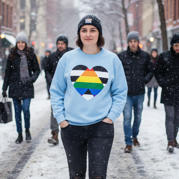 Person wearing a light blue sweatshirt with a heart-shaped Progress Pride flag graphic in falling snow