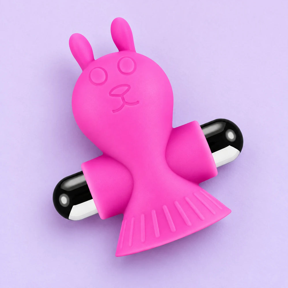 Single pink Liberating Love rabbit-shaped vibrating nipple clamp lying diagonally on lavender, showing its sculpted face and clamp ends.