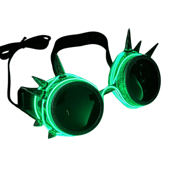 Angled view of green glowing steampunk goggles with dark lenses, spikes, and an adjustable strap