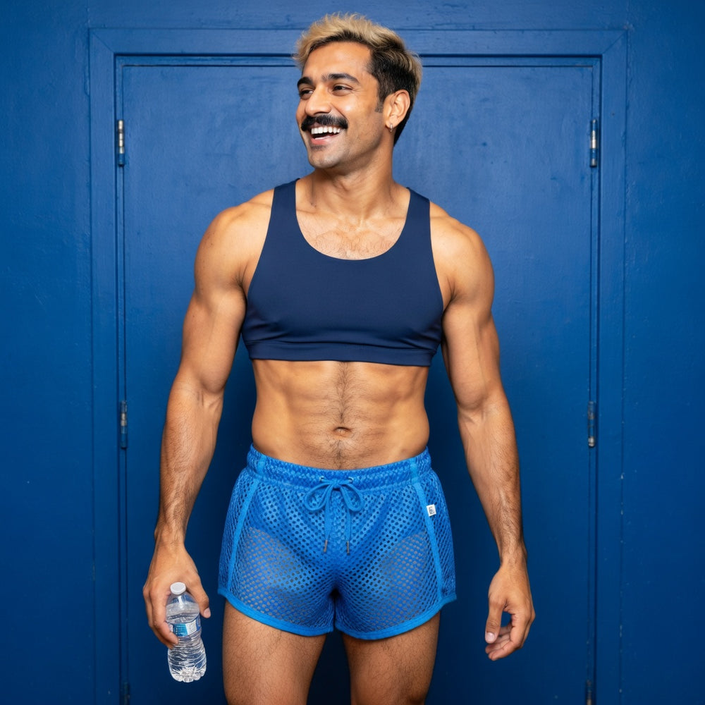 Blue loose-fit mesh boxers worn over separate opaque briefs with a cropped top in a fashion portrait.