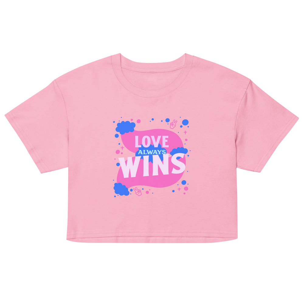 Front view of a pink crop top reading “LOVE ALWAYS WINS” in white and blue