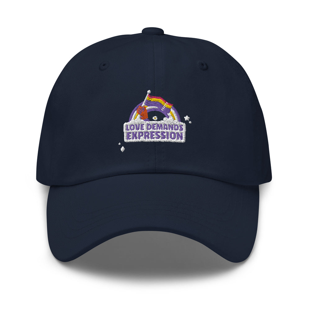 Navy Pride baseball cap with a stitched patch of a purple hand waving a rainbow flag over “LOVE DEMANDS EXPRESSION” and stars