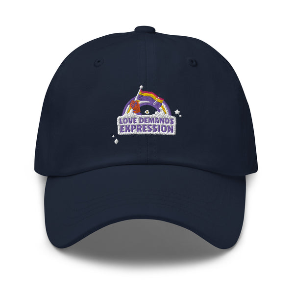 Navy Pride baseball cap with a stitched patch of a purple hand waving a rainbow flag over “LOVE DEMANDS EXPRESSION” and stars