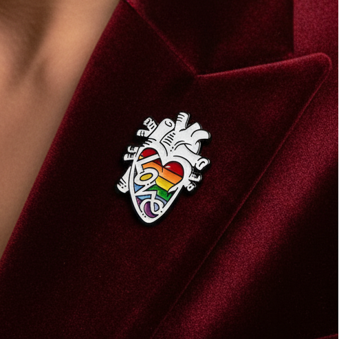 Rainbow love heart enamel pin with illustrated hands on burgundy fabric