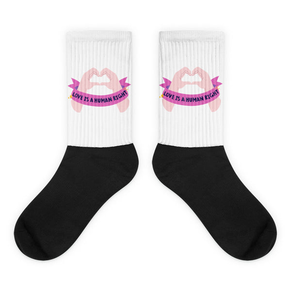 Pair of black-and-white crew socks with pink hand-heart graphics and “LOVE IS A HUMAN RIGHT” text