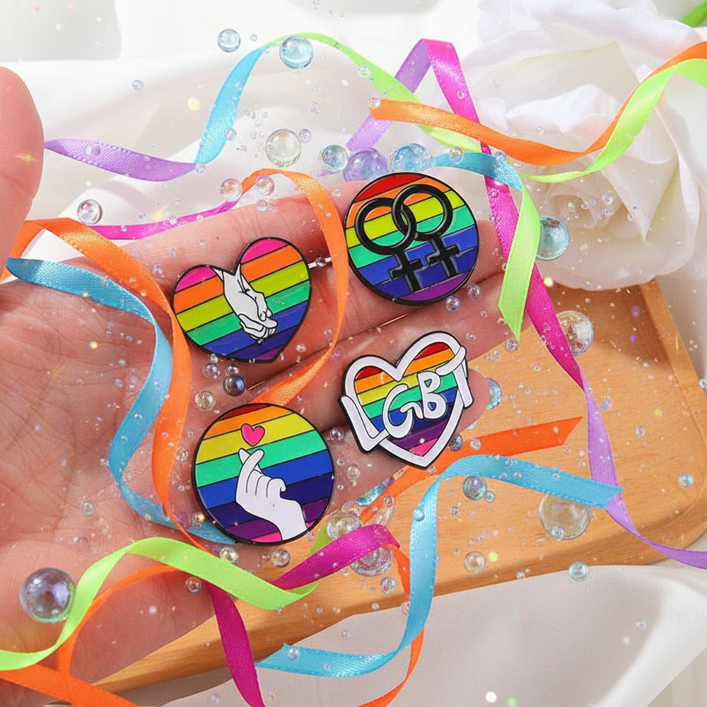 Four rainbow enamel pins displayed on a hand amid colorful ribbons and bubbles