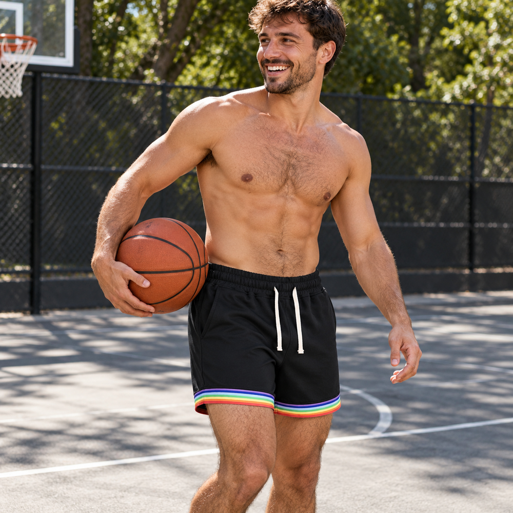 Shirtless man wearing black Love is Love basketball shorts with rainbow hems on a summer court.