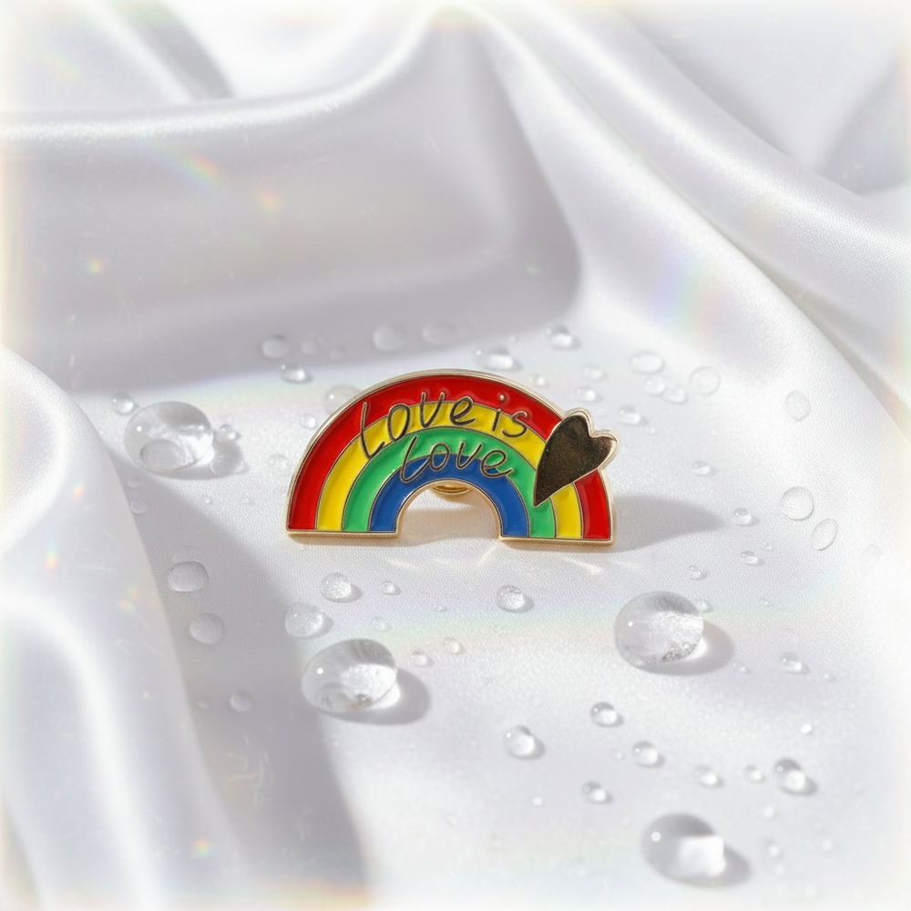 Rainbow enamel pin reading “Love is Love,” with a heart accent on white satin
