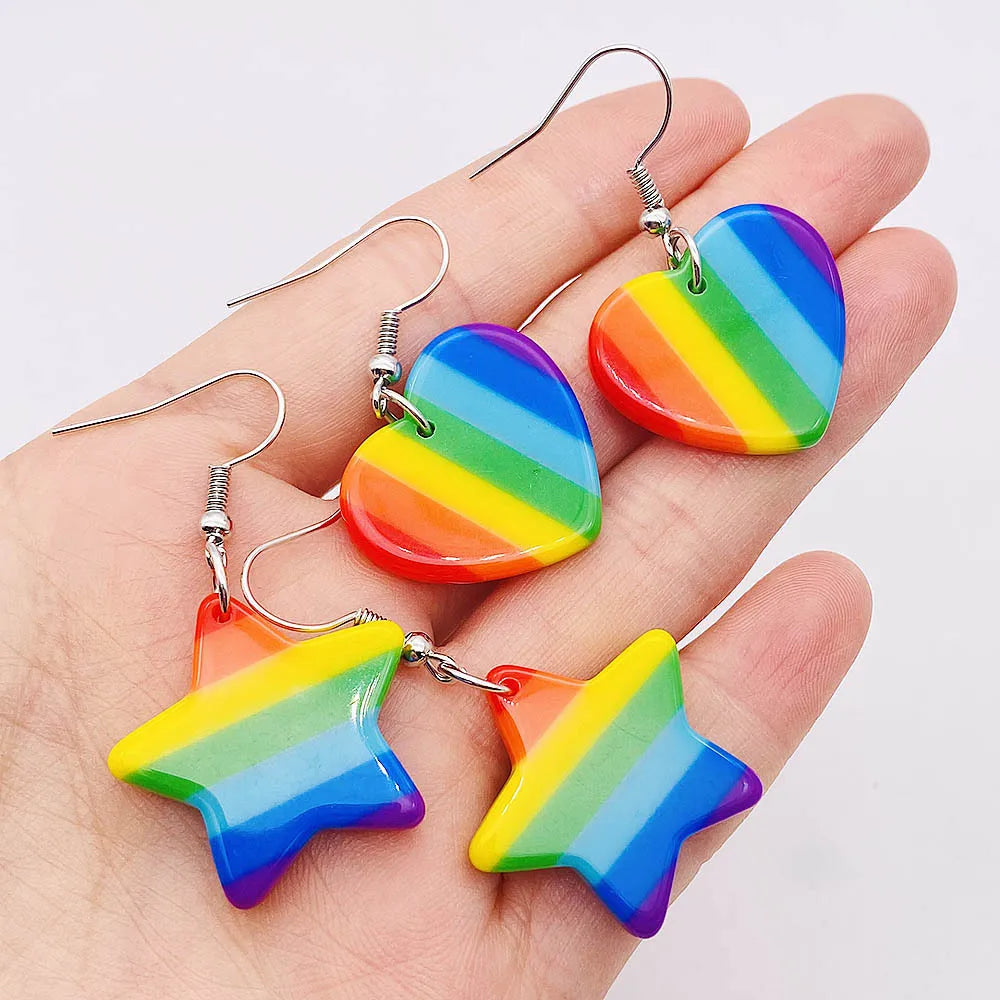 Close-up of two rainbow-striped heart and star drop earrings resting on a hand