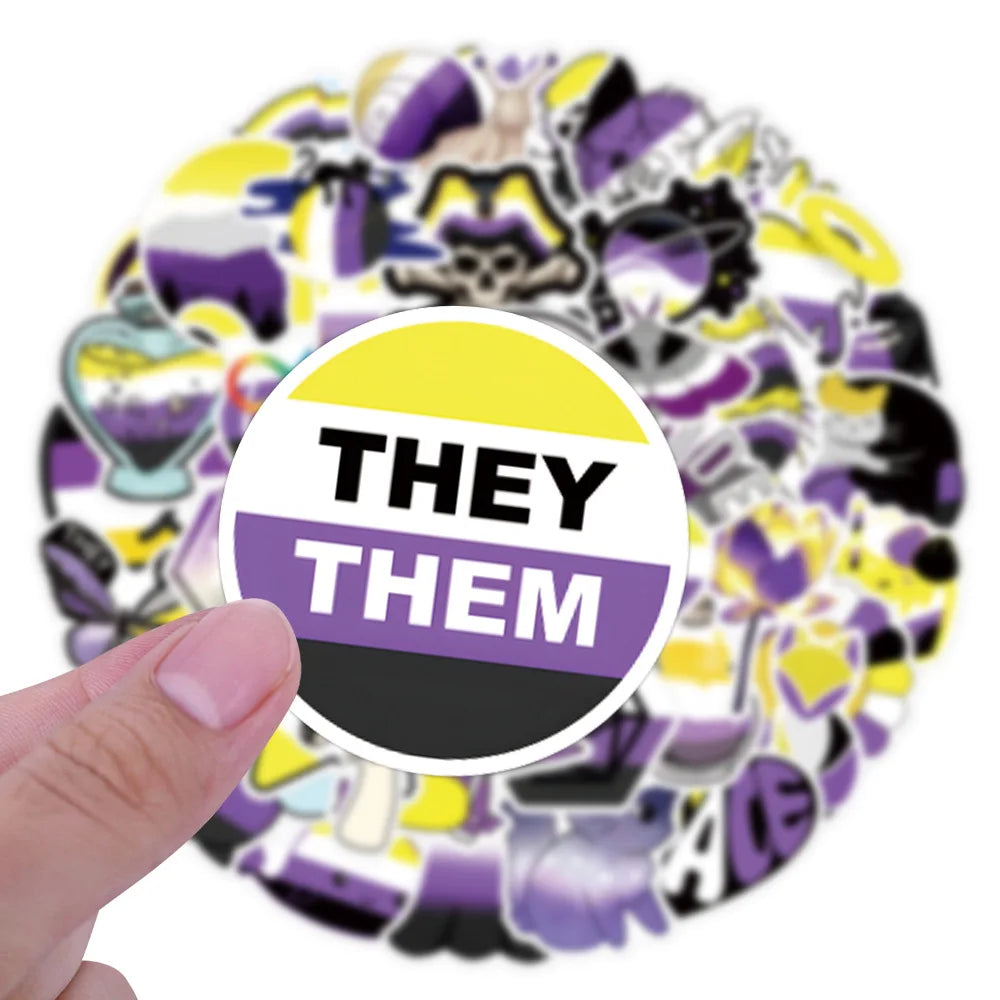 A hand holds a round non-binary pride sticker reading “THEY THEM,” with assorted stickers behind it.