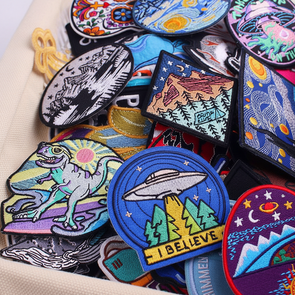 Set of 30 vibrant iron-on embroidered patches—dinosaurs, UFOs, stars, planets, more—packed in a cute beige fabric pouch.