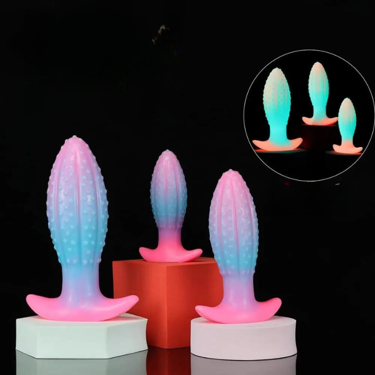 Three glowing pastel silicone butt plugs with textured shafts on display blocks