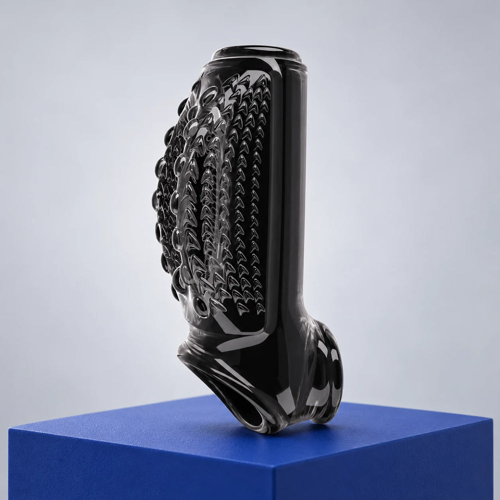 Black Magnify Master penis extension sleeve with raised circular texture and open ends on a cobalt display block.