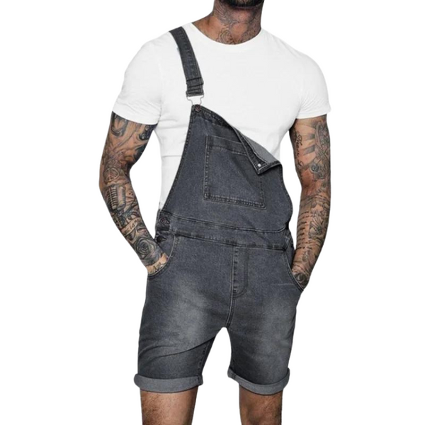 Front view of a tattooed person wearing dark denim short overalls over a white T-shirt