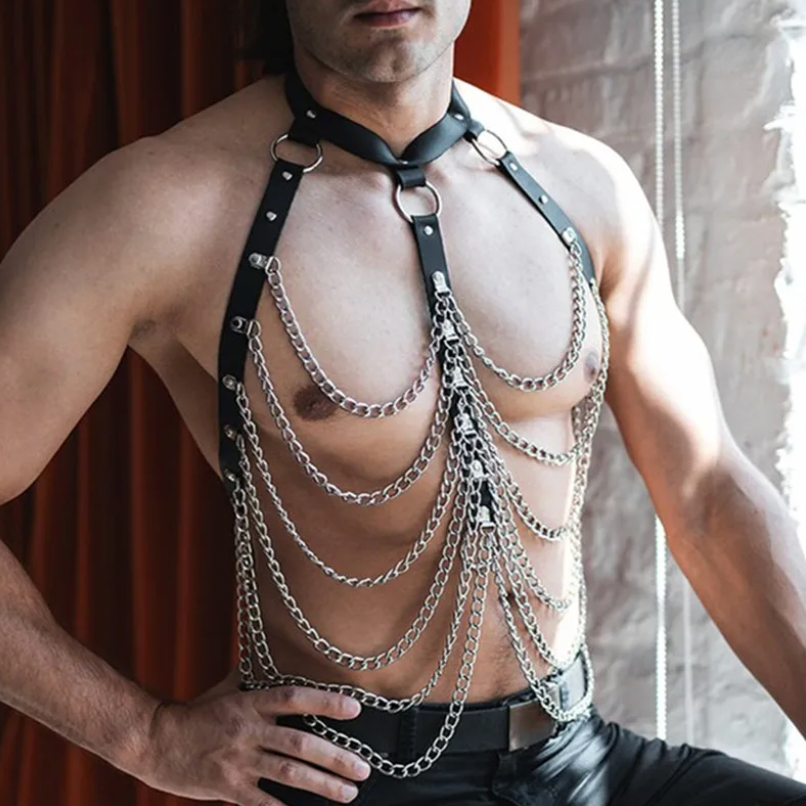 Shirtless model wearing a black leather chest harness with layered silver chains